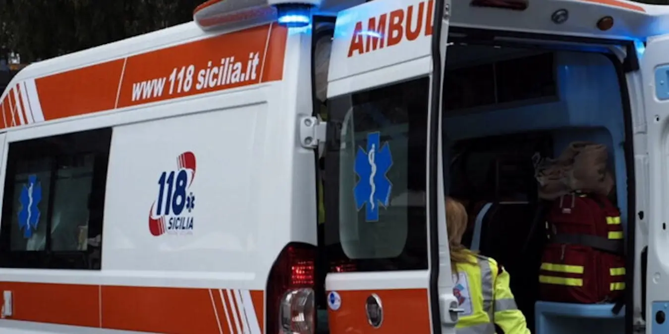 Ambulanza del 118 Sicilia con portiere posteriori aperte e operatrice sanitaria in giubbotto giallo fluorescente.