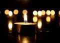 Una candela accesa su sfondo scuro con altri lumi sfocati sullo sfondo, simbolo di lutto e commemorazione