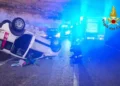 Fiat Panda bianca rovesciata sul fianco della strada di notte, con mezzo dei Vigili del Fuoco e luci blu sullo sfondo