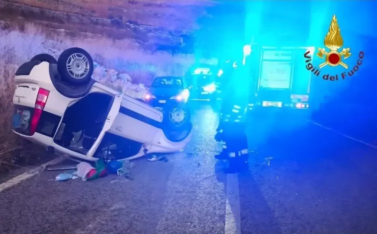Fiat Panda bianca rovesciata sul fianco della strada di notte, con mezzo dei Vigili del Fuoco e luci blu sullo sfondo