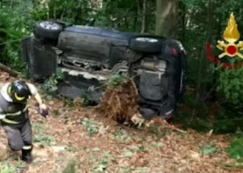 Vigile del fuoco a fianco di un'auto rovesciata sul fianco in una scarpata