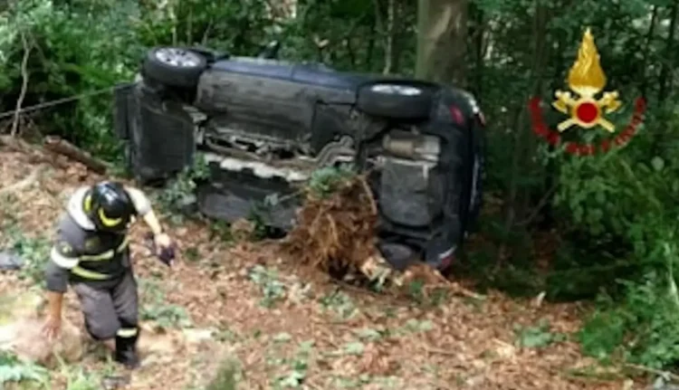 Vigile del fuoco a fianco di un'auto rovesciata sul fianco in una scarpata