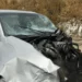 Auto di colore argento con la parte anteriore completamente distrutta e il parabrezza in frantumi, ferma sul ciglio della strada
