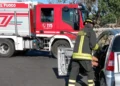 Vigile del fuoco in tenuta da intervento estrae uno sportello da un'auto incidentata, autobotte dei vigili del fuoco sullo sfondo.