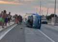 Fiat 600 rovesciata sul fianco sulla SP67 tra Marza e Pozzallo, con ambulanza e passanti sullo sfondo al tramonto