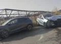 Suv scuro e utilitaria bianca con il muso danneggiato, ferme sull'asfalto dopo lo scontro, sullo sfondo una tettoia agricola.