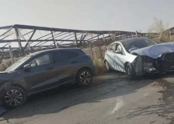 Suv scuro e utilitaria bianca con il muso danneggiato, ferme sull'asfalto dopo lo scontro, sullo sfondo una tettoia agricola.