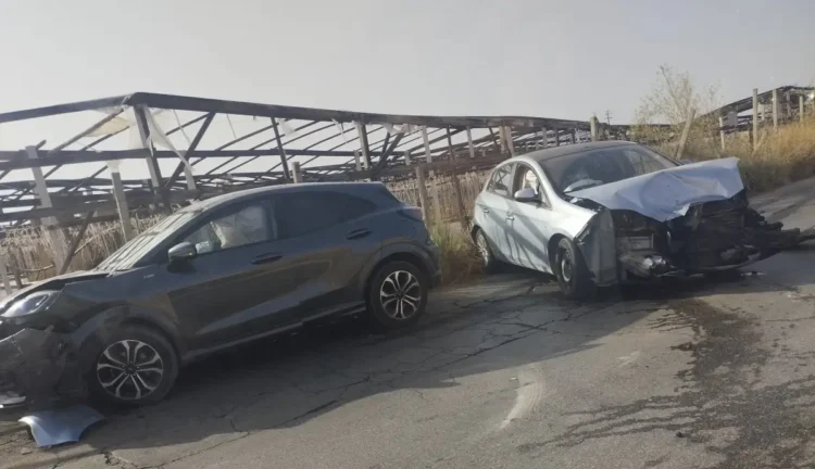 Suv scuro e utilitaria bianca con il muso danneggiato, ferme sull'asfalto dopo lo scontro, sullo sfondo una tettoia agricola.