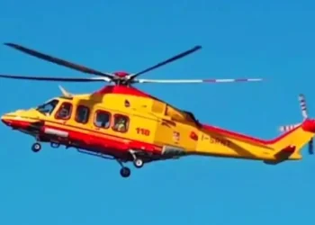 Elicottero del servizio di elisoccorso in volo su cielo azzurro, livrea gialla e rossa con scritta 118