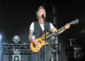 Nek suona il basso e canta al microfono durante un concerto dal vivo su un palco illuminato