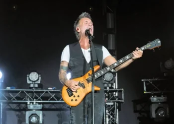 Nek suona il basso e canta al microfono durante un concerto dal vivo su un palco illuminato