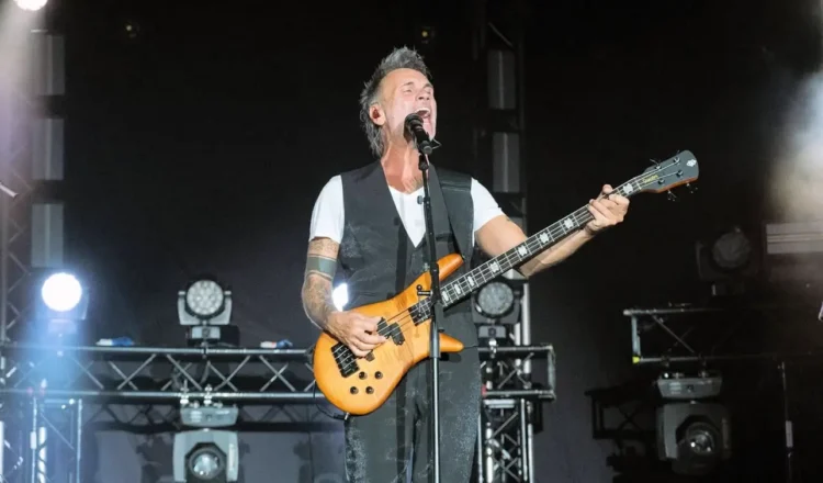 Nek suona il basso e canta al microfono durante un concerto dal vivo su un palco illuminato