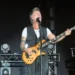 Nek suona il basso e canta al microfono durante un concerto dal vivo su un palco illuminato