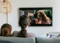 Due persone guardano la televisione sedute su un divano in un soggiorno moderno.