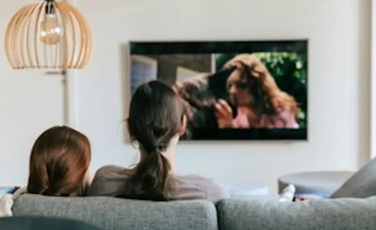 Due persone guardano la televisione sedute su un divano in un soggiorno moderno.