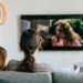 Due persone guardano la televisione sedute su un divano in un soggiorno moderno.
