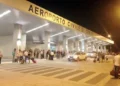 Ingresso dell'aeroporto civile di Comiso di sera, con viaggiatori e valigie davanti al terminal illuminato.
