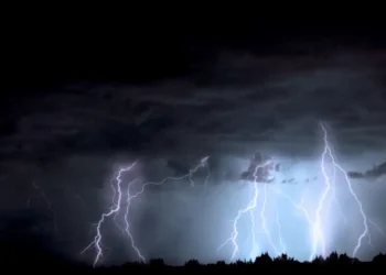 Fulmini nel cielo notturno durante un temporale, con nubi scure e silhouette di alberi all'orizzonte