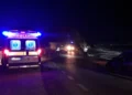 Ambulanza e auto della polizia su una strada costiera di notte, accanto a un'auto incidentata con la portiera aperta.