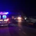 Ambulanza e auto della polizia su una strada costiera di notte, accanto a un'auto incidentata con la portiera aperta.