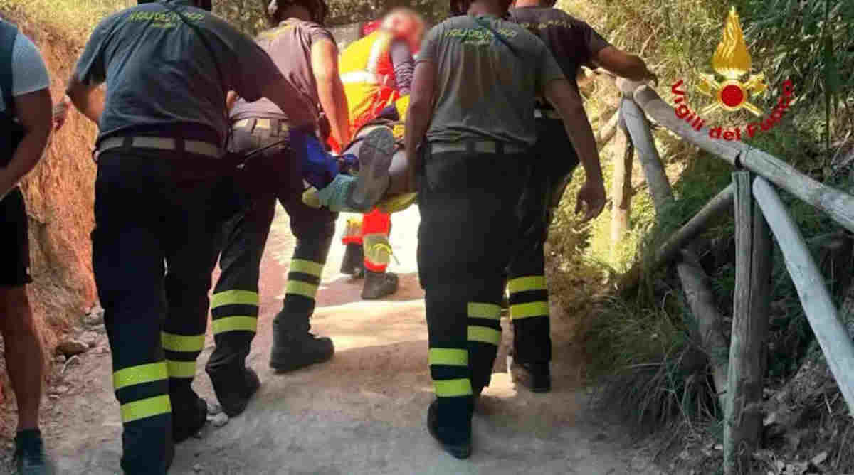 Vigili del fuoco trasportano su barella una persona soccorsa in un sentiero scosceso tra la vegetazione.