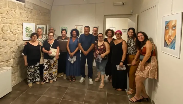 Gruppo di allievi e organizzatori posa nella sala della Fondazione Confeserfidi a Scicli, con quadri esposti alle pareti.