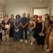 Gruppo di allievi e organizzatori posa nella sala della Fondazione Confeserfidi a Scicli, con quadri esposti alle pareti.