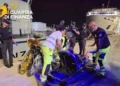 Soccorritori e Guardia di Finanza assistono un uomo su una barella in banchina di notte, traghetto sullo sfondo.