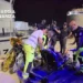Soccorritori e Guardia di Finanza assistono un uomo su una barella in banchina di notte, traghetto sullo sfondo.