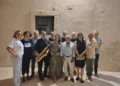 Gruppo di circa dodici persone in posa all'aperto di notte, uno dei quali regge un sassofono dorato, davanti a un muro in pietra