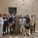 Gruppo di circa dodici persone in posa all'aperto di notte, uno dei quali regge un sassofono dorato, davanti a un muro in pietra