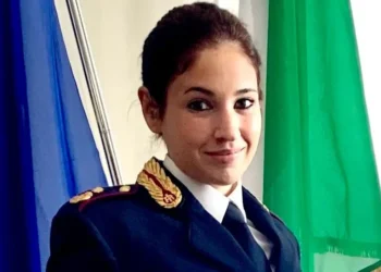Ritratto in primo piano di una donna in uniforme della Polizia di Stato, davanti a bandiere italiana ed europea.