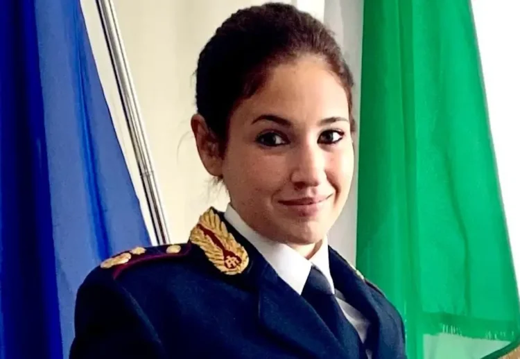 Ritratto in primo piano di una donna in uniforme della Polizia di Stato, davanti a bandiere italiana ed europea.