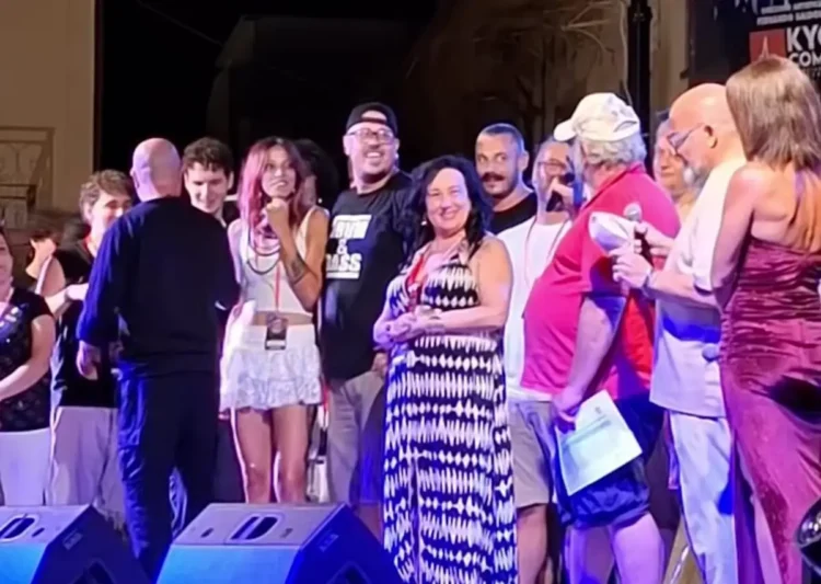Gruppo di persone sul palco durante una serata musicale, con luci colorate e monitor audio in primo piano
