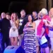 Gruppo di persone sul palco durante una serata musicale, con luci colorate e monitor audio in primo piano