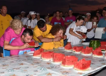 Partecipanti del Palio delle Contrade 2026 a Punta Braccetto durante la gara di mangiare anguria, circondati dal pubblico.