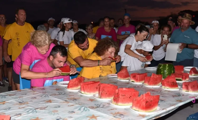 Partecipanti del Palio delle Contrade 2026 a Punta Braccetto durante la gara di mangiare anguria, circondati dal pubblico.