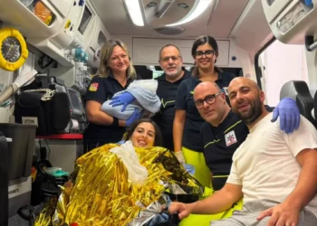 Operatori del 118 in ambulanza con la neomamma in coperta termica, il compagno e il neonato in braccio a un'operatrice.