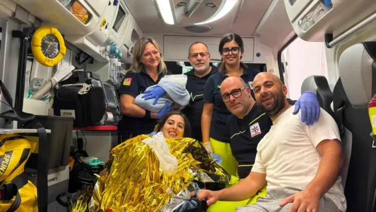 Operatori del 118 in ambulanza con la neomamma in coperta termica, il compagno e il neonato in braccio a un'operatrice.