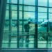 Passeggero con zaino consulta lo smartphone nell'area imbarchi di un aeroporto, aeromobili parcheggiati sul piazzale sullo sfondo.