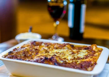 Pasta ncaciata siciliana al forno in teglia bianca con formaggio dorato e bicchiere di vino rosso