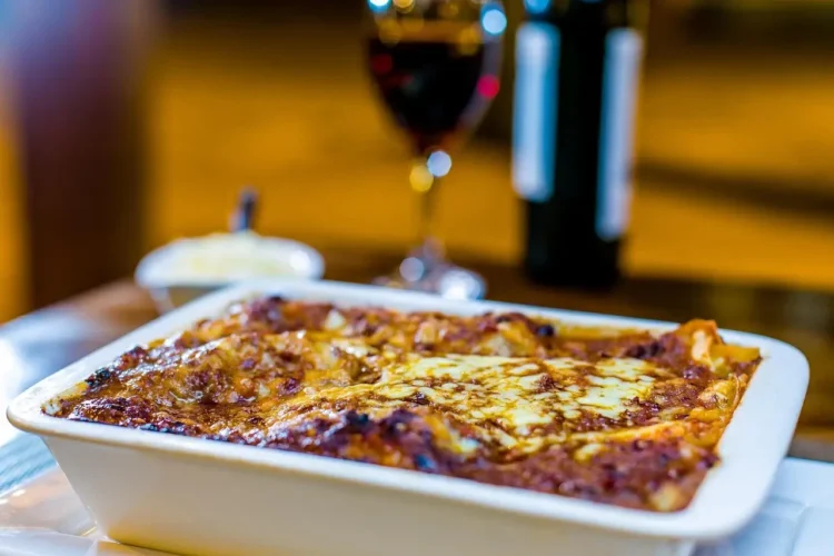 Pasta ncaciata siciliana al forno in teglia bianca con formaggio dorato e bicchiere di vino rosso