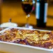 Pasta ncaciata siciliana al forno in teglia bianca con formaggio dorato e bicchiere di vino rosso