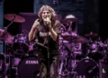 Un cantante con microfono sul palco, luci viola, batterie Tama sullo sfondo durante un concerto rock