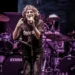 Un cantante con microfono sul palco, luci viola, batterie Tama sullo sfondo durante un concerto rock