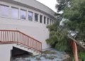 Edificio della piscina comunale di Modica con facciata curva, scala esterna e albero inclinato nel cortile in stato di abbandono