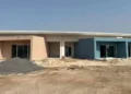 Edificio scolastico in costruzione a Marina di Ragusa con facciate color salmone e azzurro, cantiere attivo con cumuli di terra