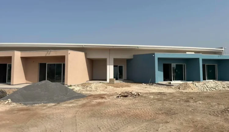 Edificio scolastico in costruzione a Marina di Ragusa con facciate color salmone e azzurro, cantiere attivo con cumuli di terra