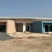 Edificio scolastico in costruzione a Marina di Ragusa con facciate color salmone e azzurro, cantiere attivo con cumuli di terra