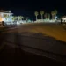 Piazzetta del porto turistico di Marina di Ragusa di notte, con gran parte della pavimentazione in penombra e palme illuminate sullo sfondo.